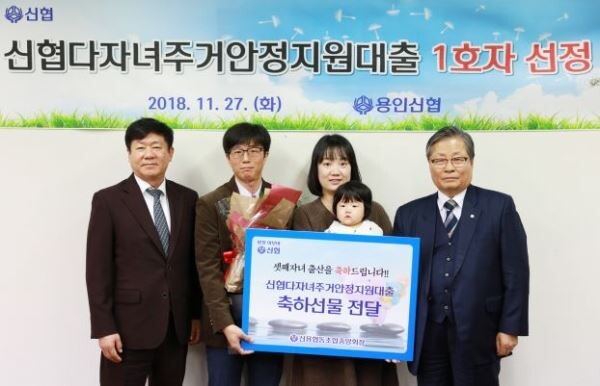 신협은 다자녀지원대출 1호 탄생을 축하하고자 해당 가정이 조합원으로 있는 용인신협에서 기념행사를 개최하고 소정의 상품을 전달했다. 사진 맨 좌측이 김윤식 신협중앙회장, 맨 우측이 김일용 용인신협 이사장이며, 가운데가 다자녀가정 부모와 셋째 자녀이다.