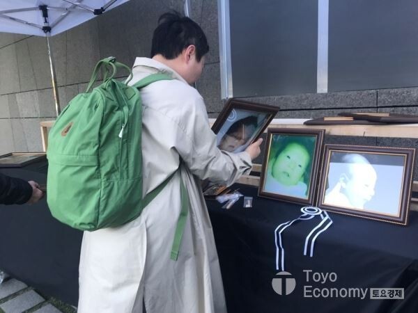 ▲2일 서울 여의도에 위치한 옥시레킷벤키저 본사앞에서 가습기살균제 피해자와 유족들이 기자회견을 가졌다. 피해자가 분향소를 설치하며 사망자의 사진을 바라보고 있다. [사진=김자혜 기자]